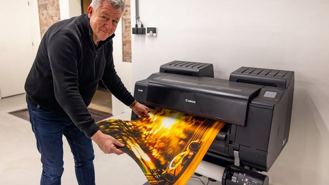 Motorsport photographer Frits van Eldik holds a large print of a vehicle as it emerges from a Canon large format printer.
