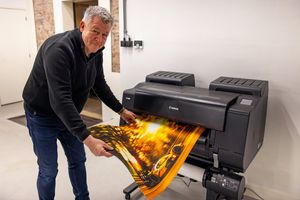 Фотограф гонок Фритц ван Элдик берет руками большую печатную фотографию болида, появляющуюся из широкоформатного принтера Canon.