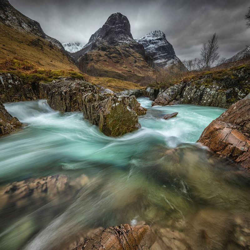 A one-second exposure of a fast flowing river surrounded by mountains. The long exposure has blurred the movement of the water.