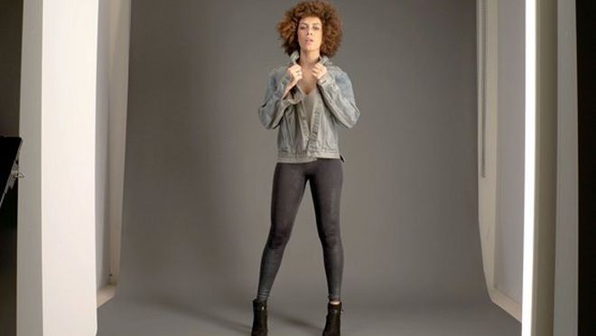 Eine Modeaufnahme für ein Online-Bekleidungsunternehmen, bei der eine Frau in Jeansjacke und schwarzer Strumpfhose in einem Fotostudio posiert.