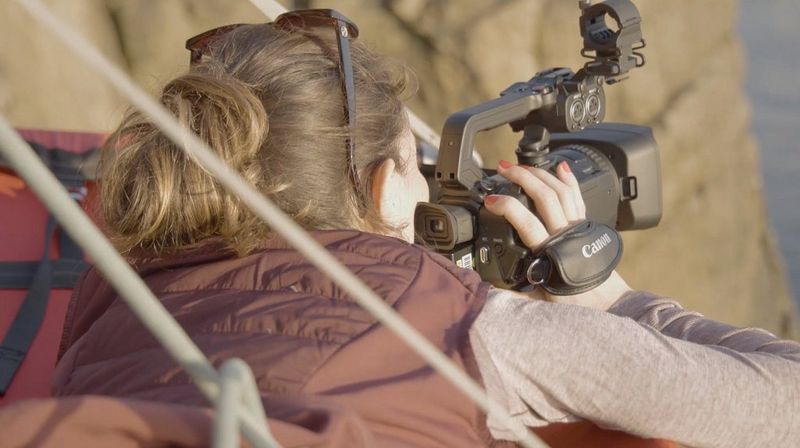 La journaliste Elisa Iannacone en train de filmer sur le bord d'une falaise avec un caméscope Canon XA55.
