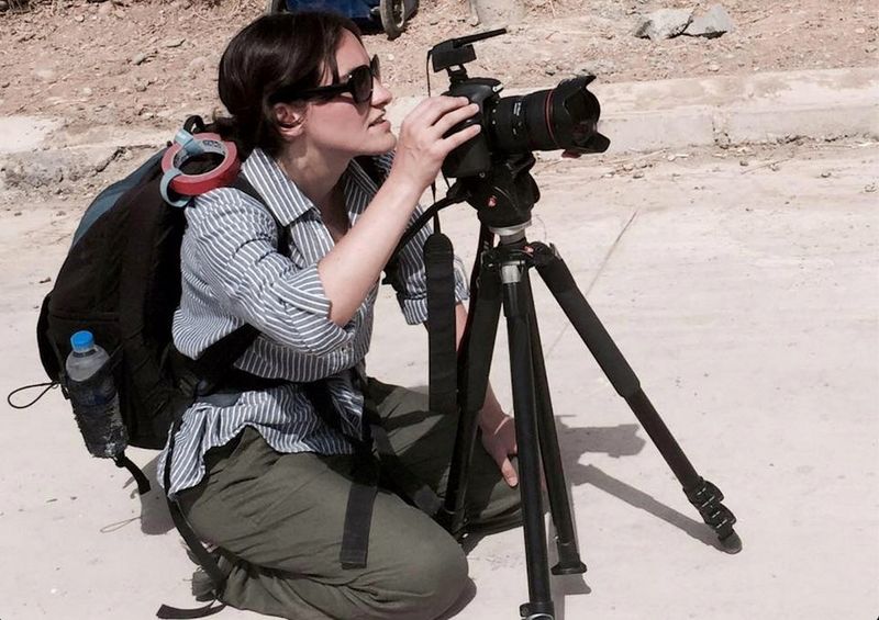 Elisa Iannacone agenouillée derrière un trépied accueillant un appareil photo Canon dans une rue poussiéreuse, en Irak.