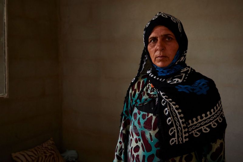 Une réfugiée irakienne portant une robe à motifs et un foulard sur un arrière-plan foncé simple.