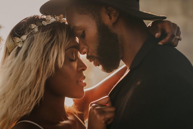 A newlywed couple embracing, with their eyes closed and their foreheads touching. The bride is wearing a flower crown in her hair. 