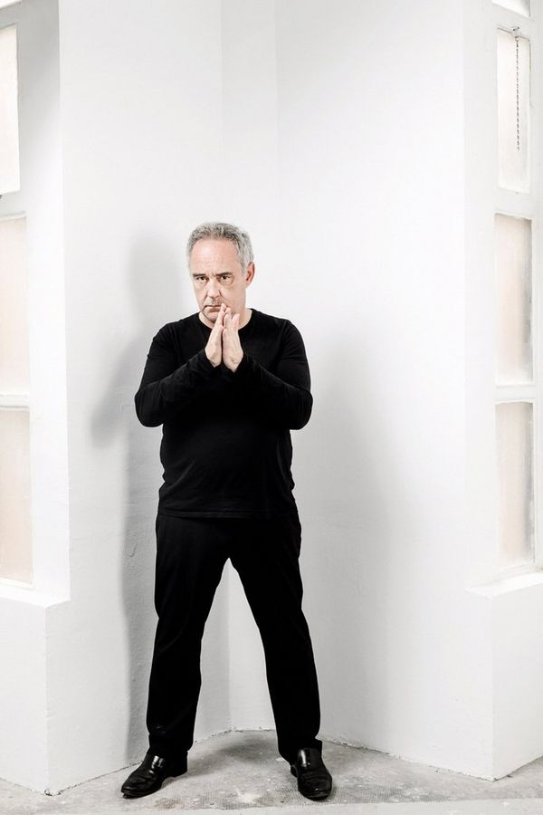 A portrait of Spanish Chef Ferran Adri dressed in black and standing against a white wall.