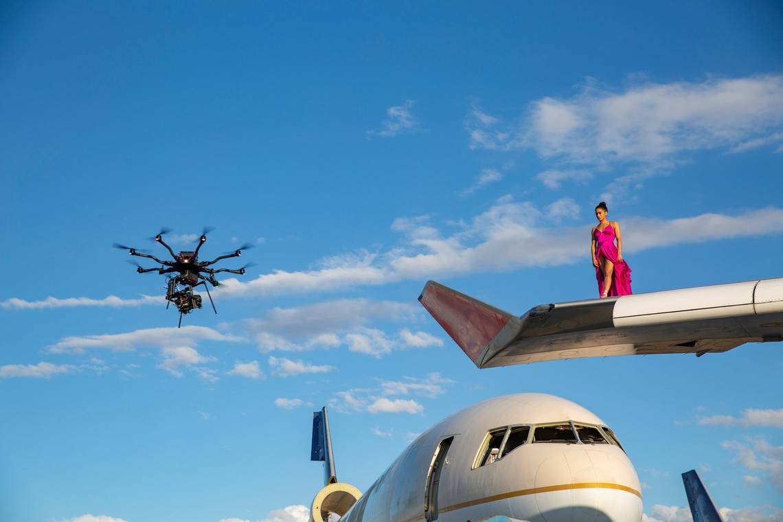 A Canon EOS C300 Mark III attached to a drone, filming a ballerina in a bright fuchsia dress standing on the wing of a 747. 