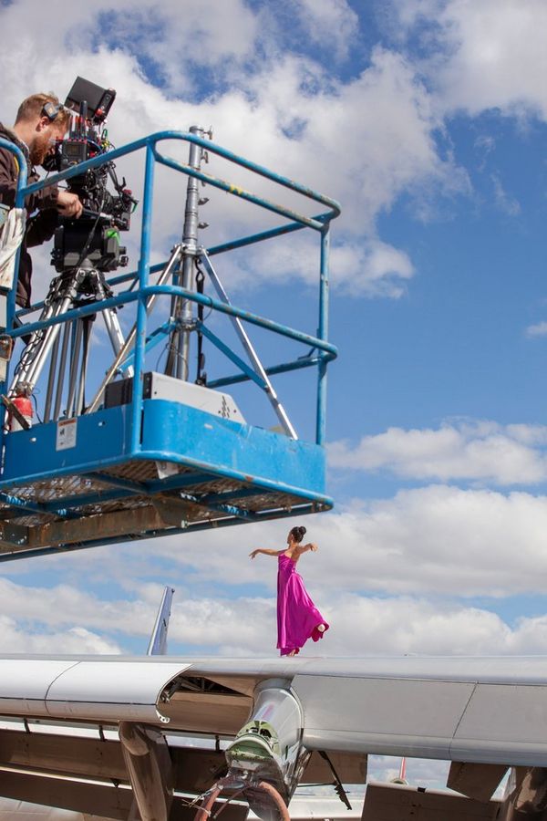 A ballerina dancing on the wing of an aircraft being filmed by a cameraman on a forklift. 