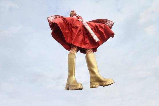 Une mannequin portant de grosses bottes dorées et une robe rouge voluptueuse est suspendue dans les airs. Photo prise par Nana Simelius avec un Canon EOS R6 Mark II.