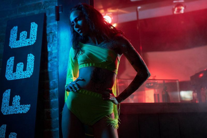 A female model wears a neon yellow bikini in a blue and red-lit room. Fashion photo by Jaroslav Monchak on a Canon EOS R with a Canon RF 50mm F1.2 L USM lens.
