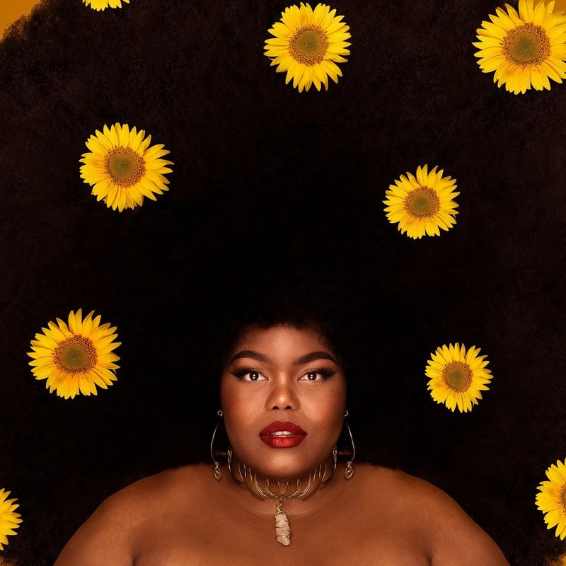 A portrait of a woman with a large afro filled with sunflowers. 