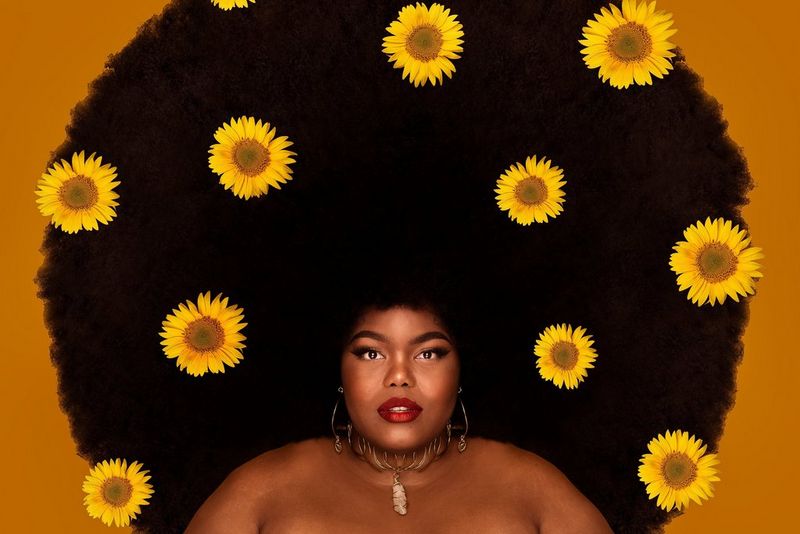 A portrait of a woman with a large afro filled with sunflowers. 