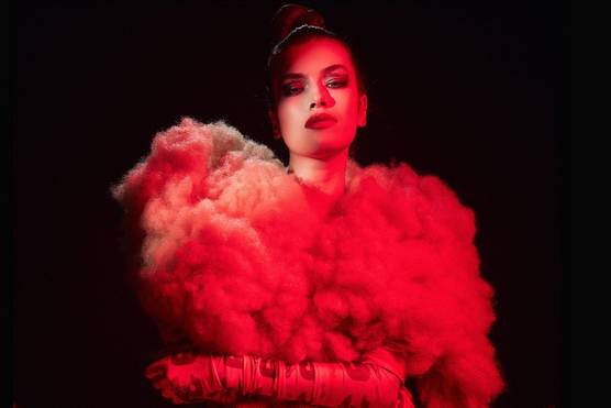 A portrait of a model illuminated in red against a dark background. The model is wearing an extravagant top made of what looks like fluffy cotton wool.