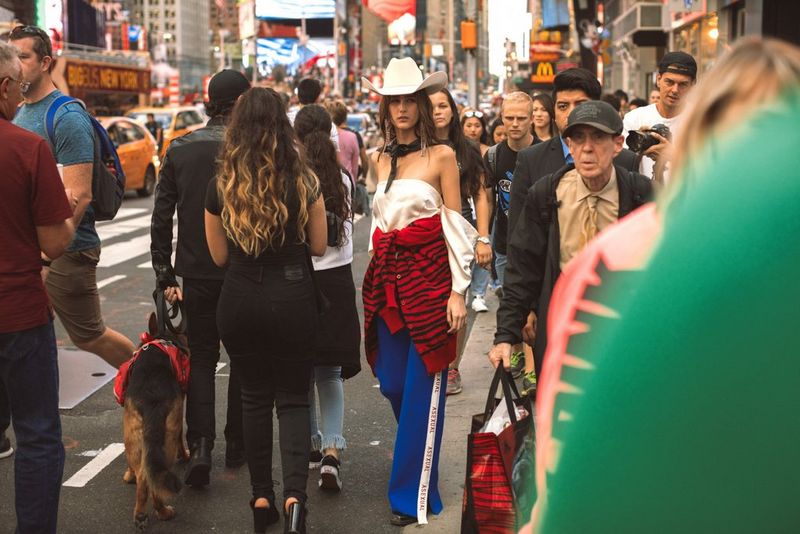 A fashion model in a cowboy hat walking down a crowded New York street.