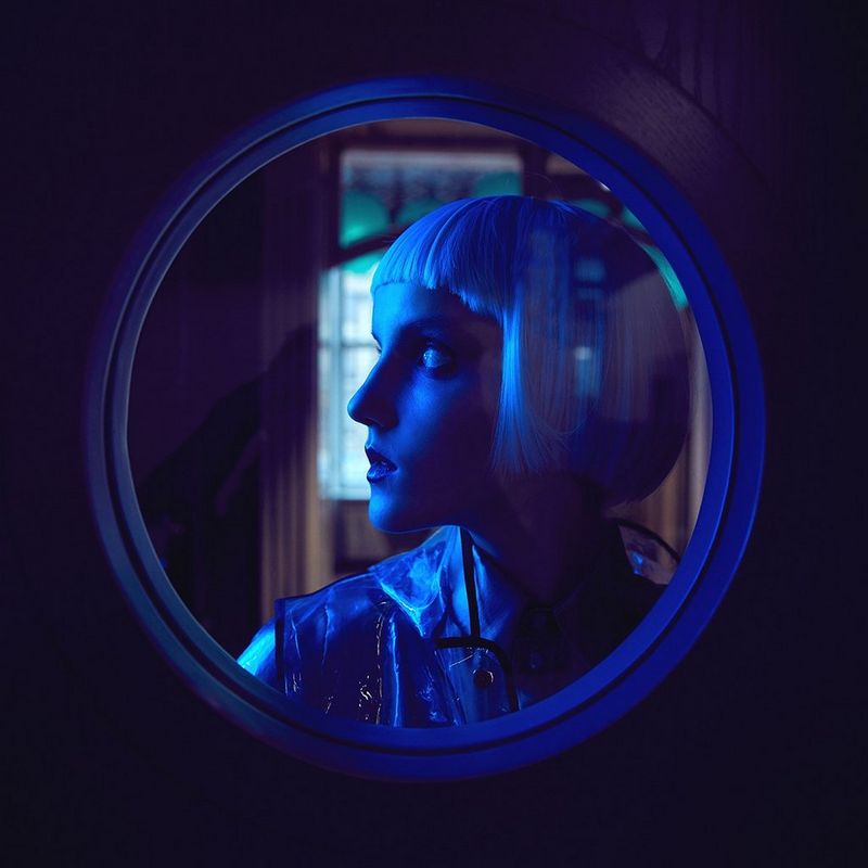 A profile of a woman behind a circular window, shot with a blue gel filter.
