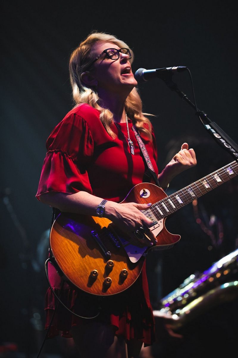 A woman wearing a red dress and holding a guitar sings into a microphone.