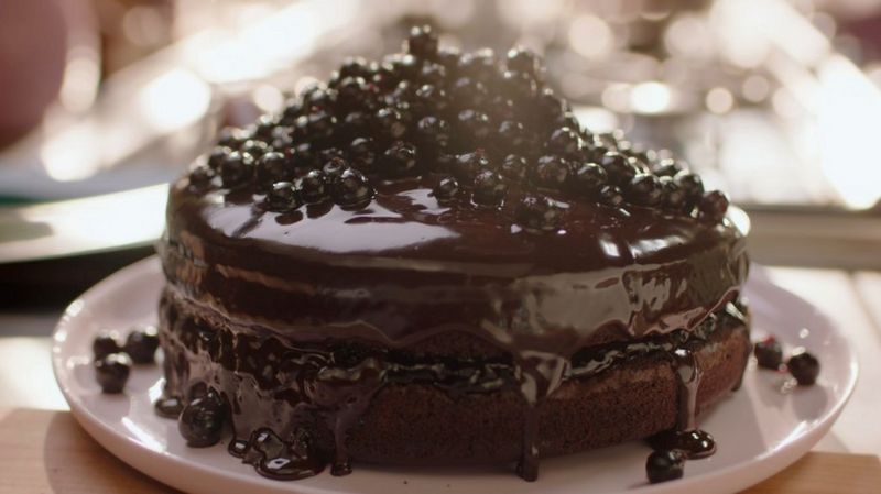 A rich chocolate cake covered in a glossy chocolate sauce and topped with blackcurrants.