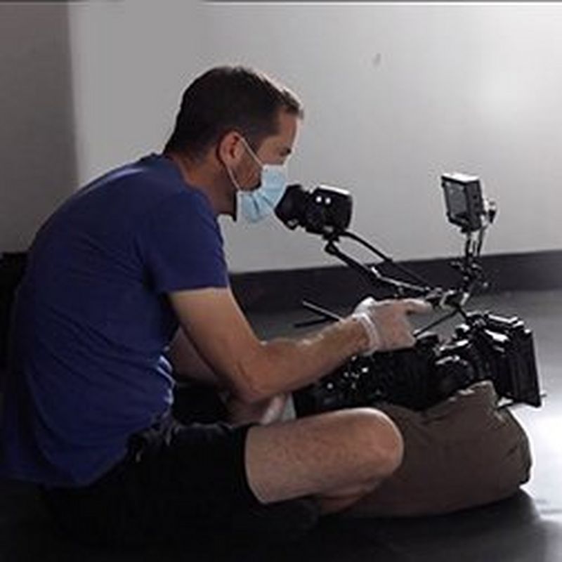 A man wearing a face mask sitting on the floor filming in a hospital. 