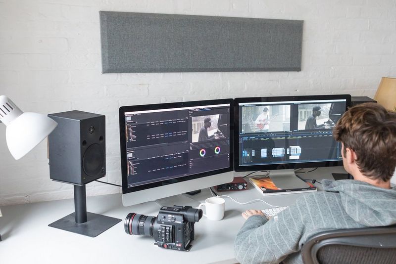 Shot from behind, a man sits an editing desk in front of two monitors. A Canon EOS C200 cinema camera is on the desk beside him.