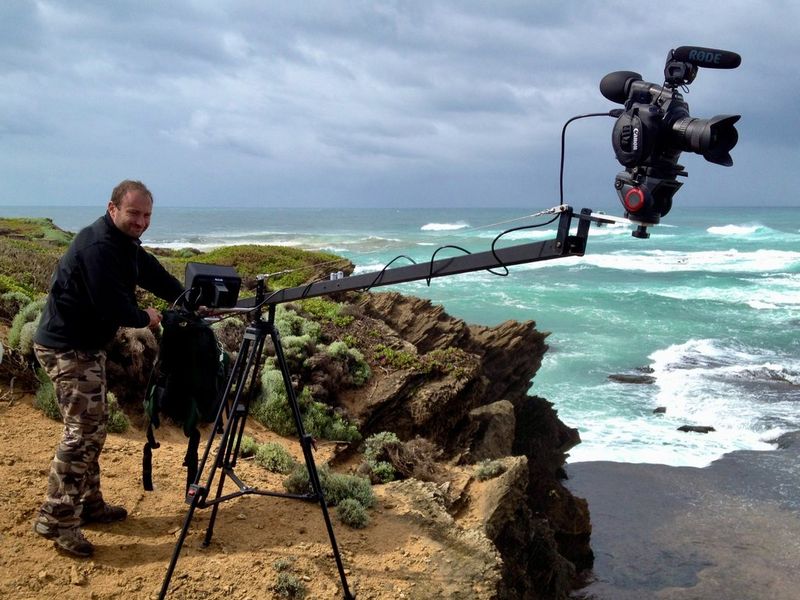 Roberto Palozzi standing on a clifftop overlooking the shore filming with a Canon camera mounted on a long arm rig. 