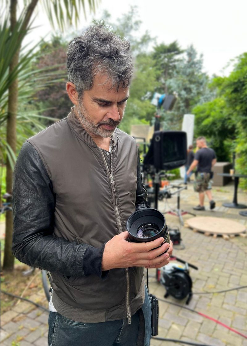 DoP Ian Murray looks down at a Canon FD 135mm prime lens, a shoot setup in an outdoor space behind him.