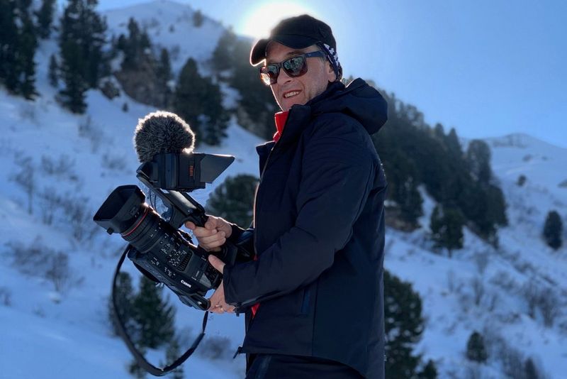 Мужчина в зимней одежде на заснеженном склоне горы с видеокамерой Canon XF705.