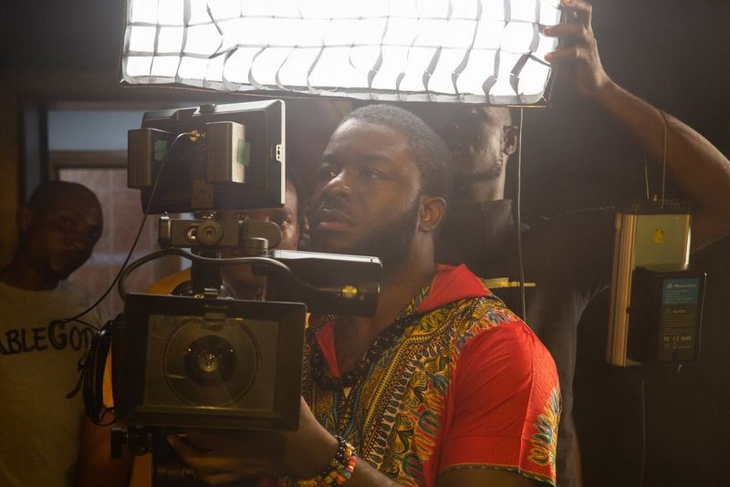 Le réalisateur Daniel Ehimen en chemise orange à motifs, actionnant une caméra.
