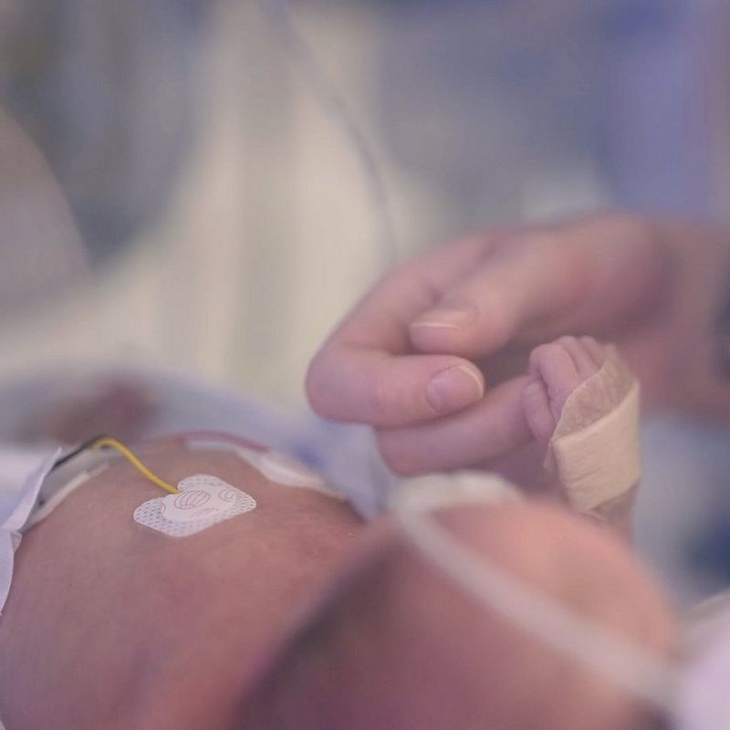 Close-up of an adult hand holding the hand of a newborn baby.