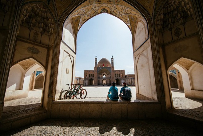 Два маунтинбайкера сидят в арке перед мечетью, повернувшись спиной к камере.