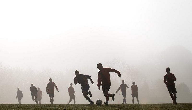 Силуэты игроков на фотографии, созданной во время футбольного матча; такого эффекта удалось добиться благодаря лучам солнца, пробивающимся через утренний туман.