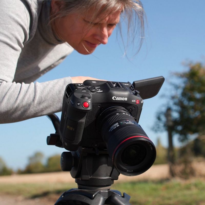 Cinematographer Tania Freimuth leans over a Canon EOS C70, which is attached to a tripod. 