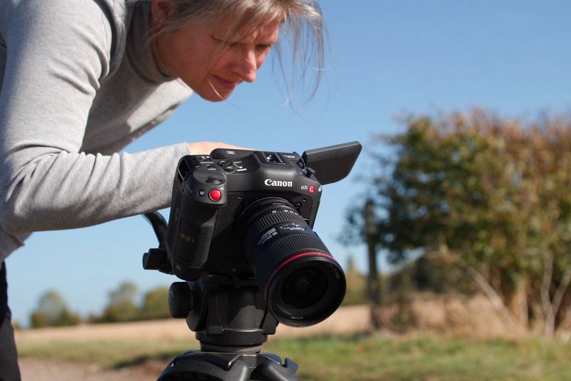 A woman, Tania Freimuth, looks at the vari-angle screen on her Canon EOS R5 C camera, while standing outdoors on a field. 