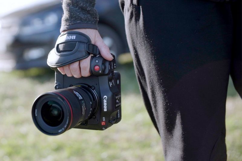 A person holds a Canon EOS C70 camera down at the side of their body.