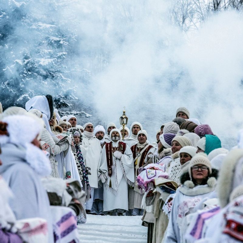 Members of the Church of the Last Testament stand in white robes in front of snow-covered trees.