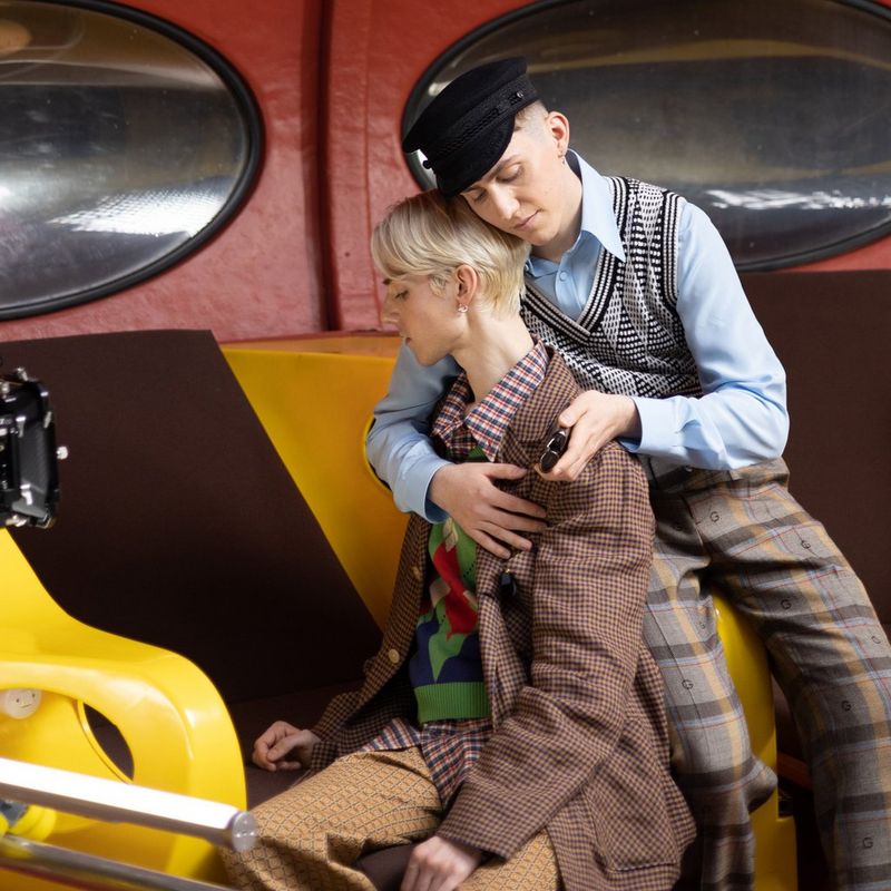 Two people sit together in front of a Canon Cinema camera on a shoot set, one person with their arm around the other from the back.