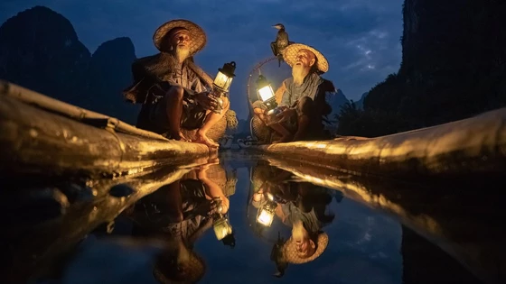 Two Chinese cormorant fishermen sat in long boats with lanterns.