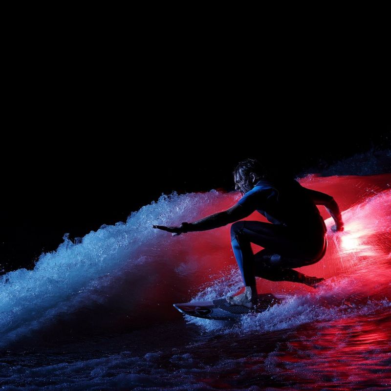 Wakesurfer Andy Schmahl rides a wave, illuminated by the glow of an orange flare he is holding. 