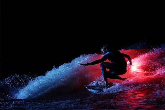 Wakesurfer Andy Schmahl rides a wave, illuminated by the the glow of an orange flare he is holding.