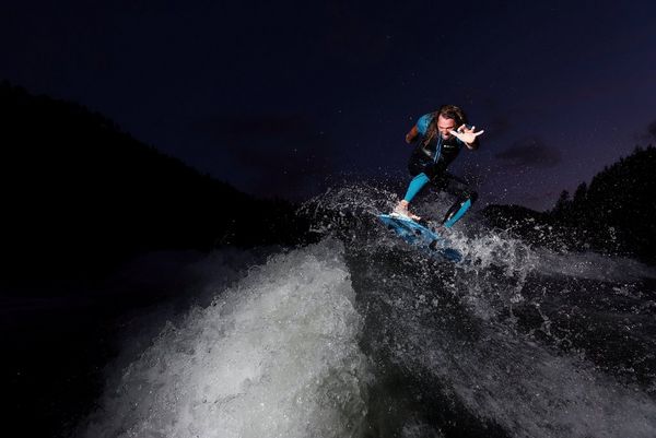 Wakesurfer Andy Schmahl rides the crest of a wave, his arms outstretched.