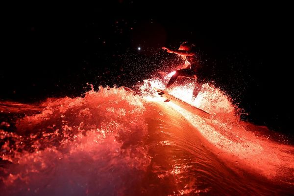 Wakesurfer Andy Schmahl rides a wave holding a red flare in his hand.