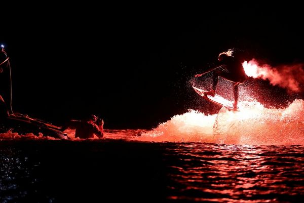 Extreme sports photographer Richard Walch stands chest deep in a lake photographing a wakesurfer carrying a flare.