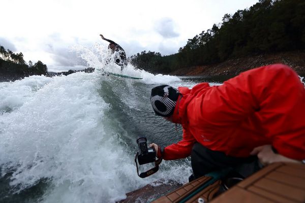 Extreme sports photographer Richard Walch leans off the back of a boat holding the camera low to capture the wakesurfer following behind.