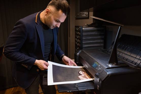 Photographer Sanjay Jogia leans over a Canon imagePROGRAF PRO-1000 printer, as a large print of a photograph of a woman with long dark hair emerges.