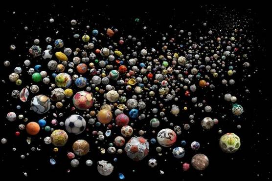 A large number of footballs in varying states of decay are pictured, as if floating, against a black background.