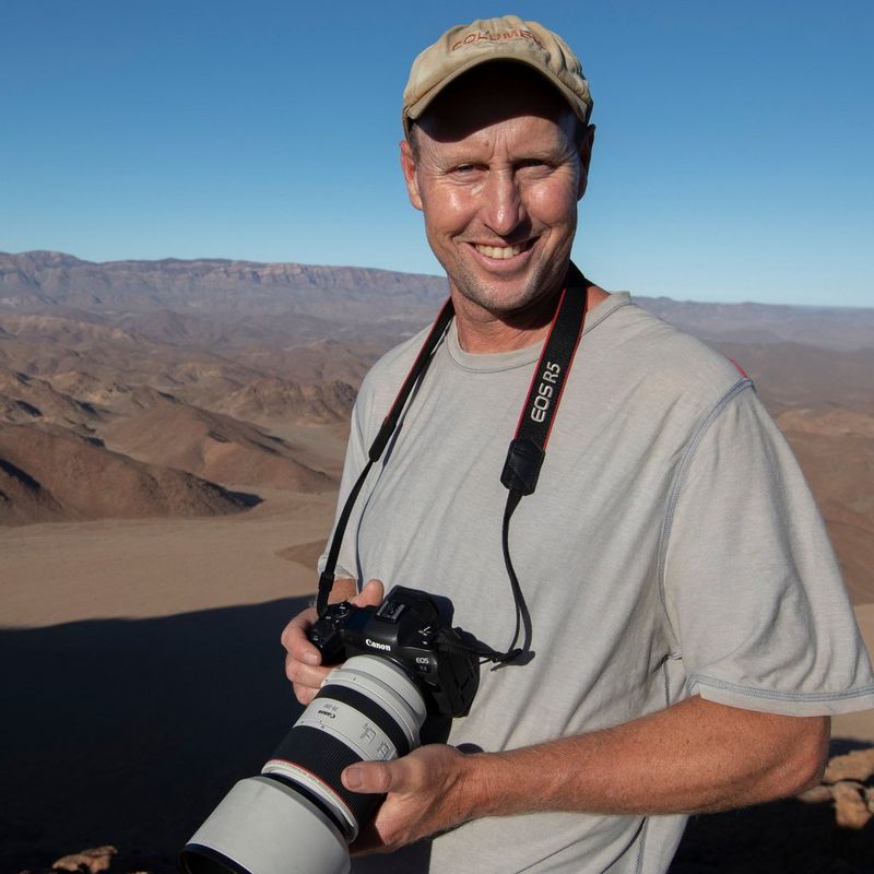Fine art wildlife photographer Chris Fallows pictured in a desert holding a Canon EOS R5 with a Canon RF 70-200mm F2.8L IS USM lens.