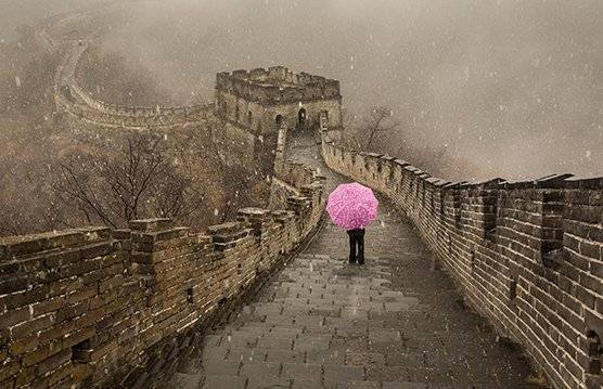 Snow falls on a figure standing on the Great Wall of China holding an eye-catching pink umbrella. Taken by Joel Santos. 
