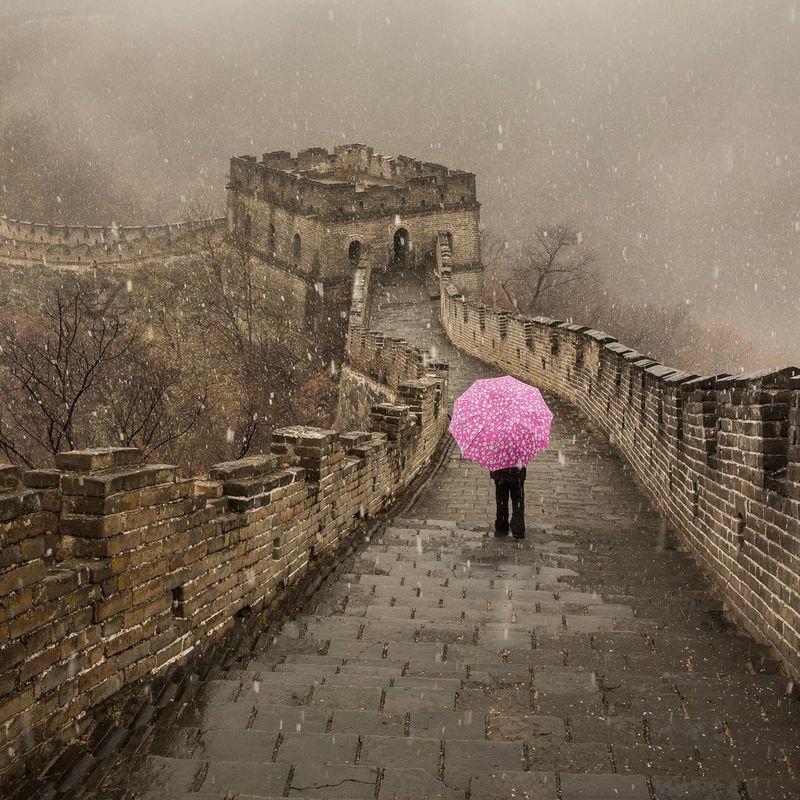 Snow falls on a figure standing on the Great Wall of China holding an eye-catching pink umbrella. Taken by Joel Santos. 