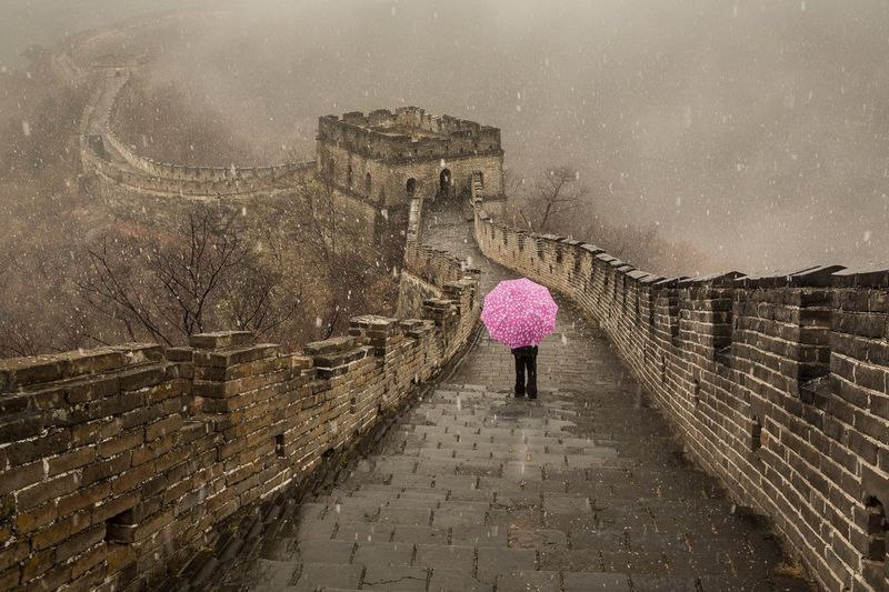 Snow falls on a figure standing on the Great Wall of China holding an eye-catching pink umbrella. Taken by Joel Santos.