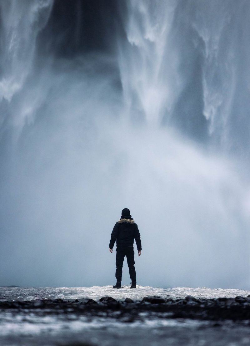 Harrison Brown stands facing a waterfall, his silhouette captured from behind.