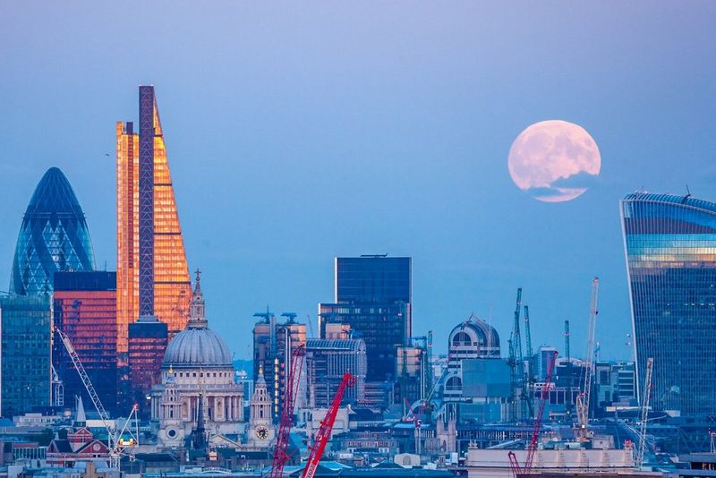 На фотографии, сделанной Джеймсом Бернсом, над городским пейзажем Лондона возвышается Луна в белых тонах.