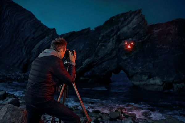 Rob Payne photographs a rocky coastline. A drone is being used to "paint" red light onto the surface of the water.